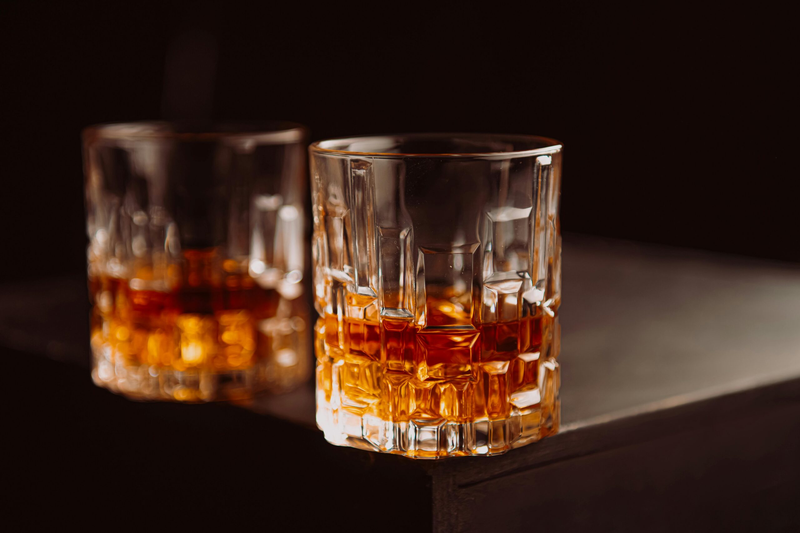 Crystal glasses filled with whiskey on a dark wooden surface, highlighting texture and color.
